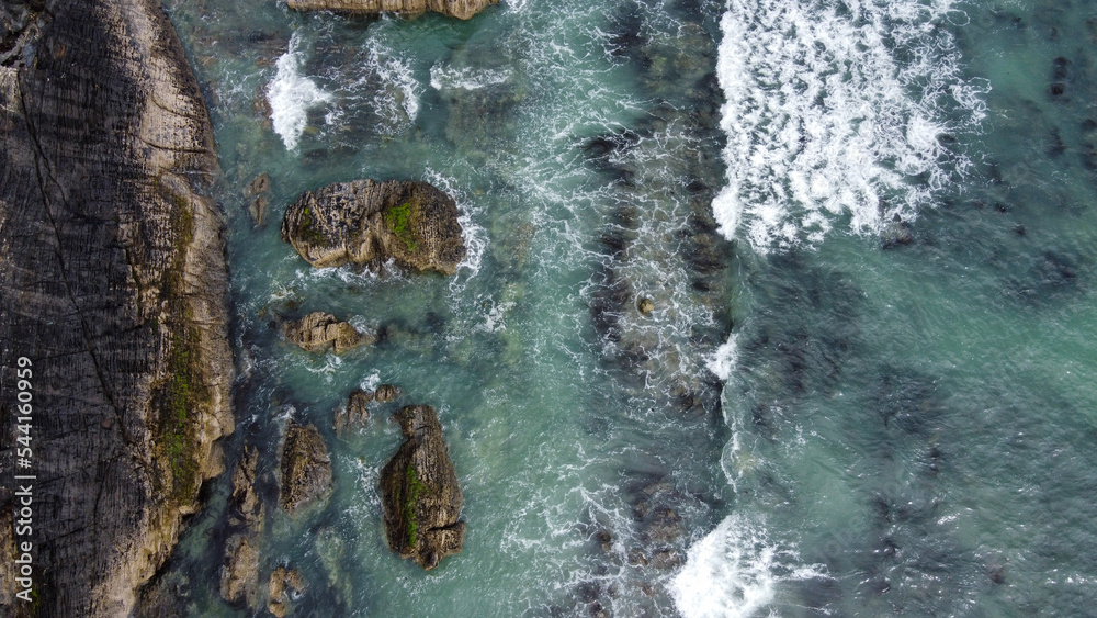 Waves break on the rocky shore of the Celtic Sea, top view. White foam on the waves. The coastline of the Atlantic. Turquoise sea water. Breathtaking seaside landscape. Waves break on the rocky shore of the Celtic Sea, top view. White foam on the waves. The coastline of the Atlantic. Turquoise sea water. Breathtaking seaside landscape.