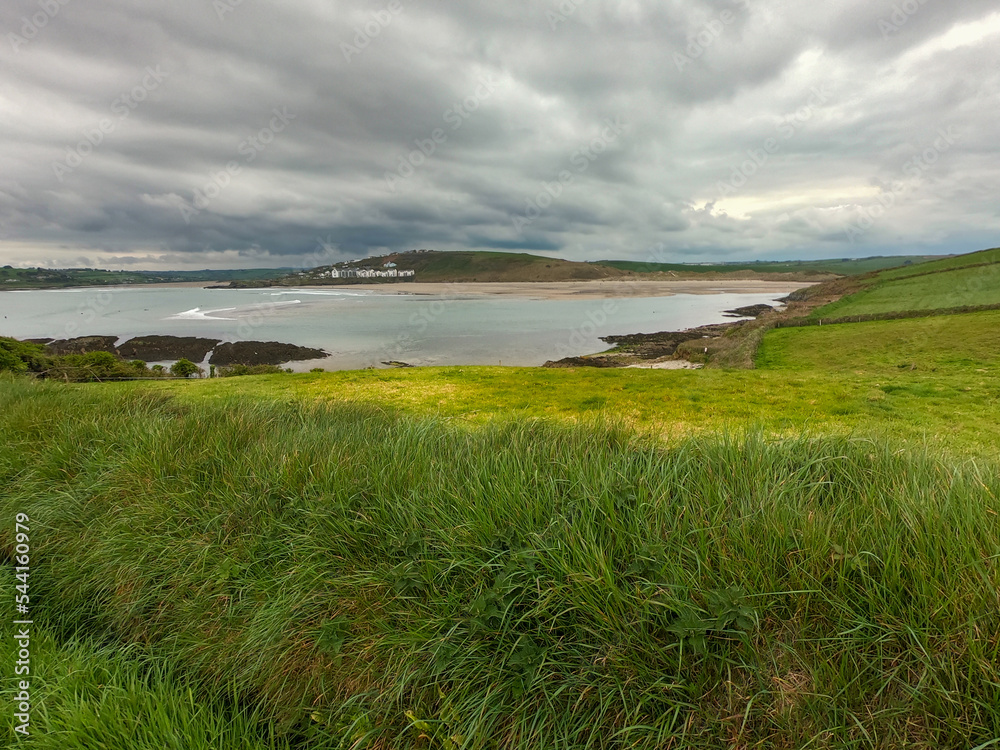 Thick green grass on a hill near the sea bay. Cloudy sky over Clonakilty Bay, seascape. Drone point of view.