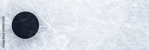 Black old rubber puck on ice background. Closeup. Wide banner. Top down view. Empty place for text. photo
