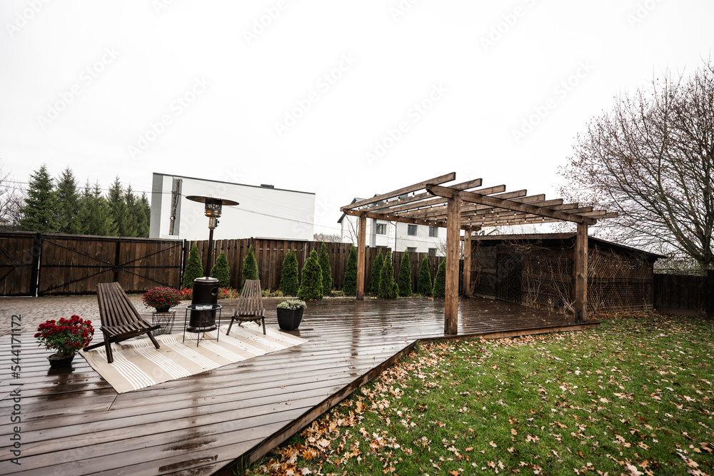Stainless steel metal gas outdoor patio heater with wooden chairs and pot with flowers at wet terrace. Place to relax.
