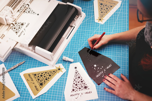 Photography woman with painted nails works on a christmas graphic cut from black adhesive vinyl foil