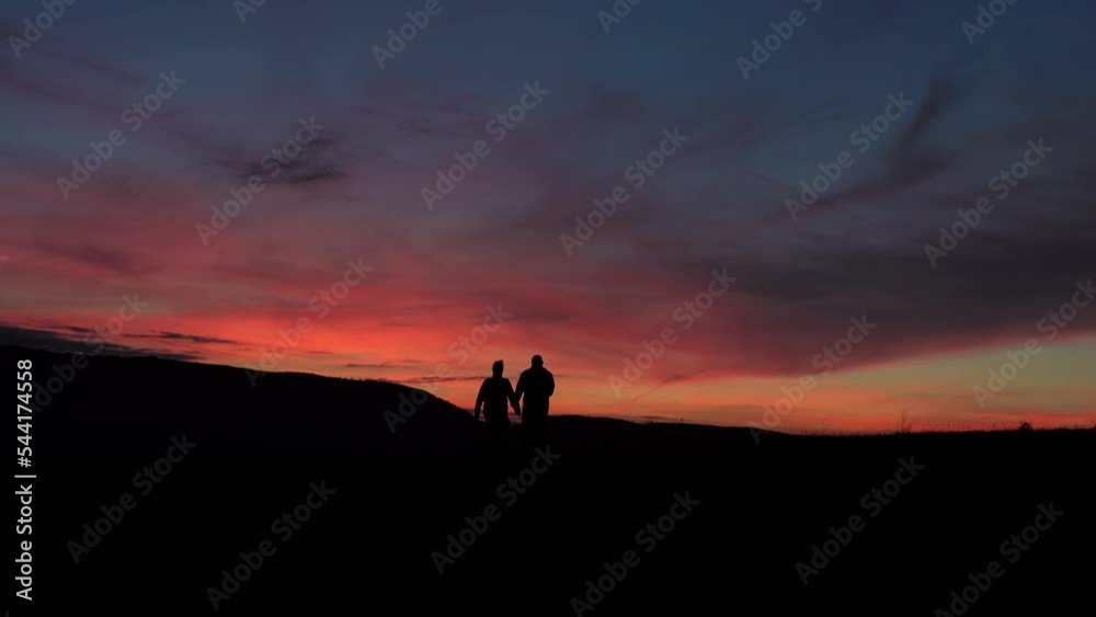 Silhouette Couple walking hand in hand on a mountain, at sunset Silhouette Couple walking hand in hand on a mountain, at sunset