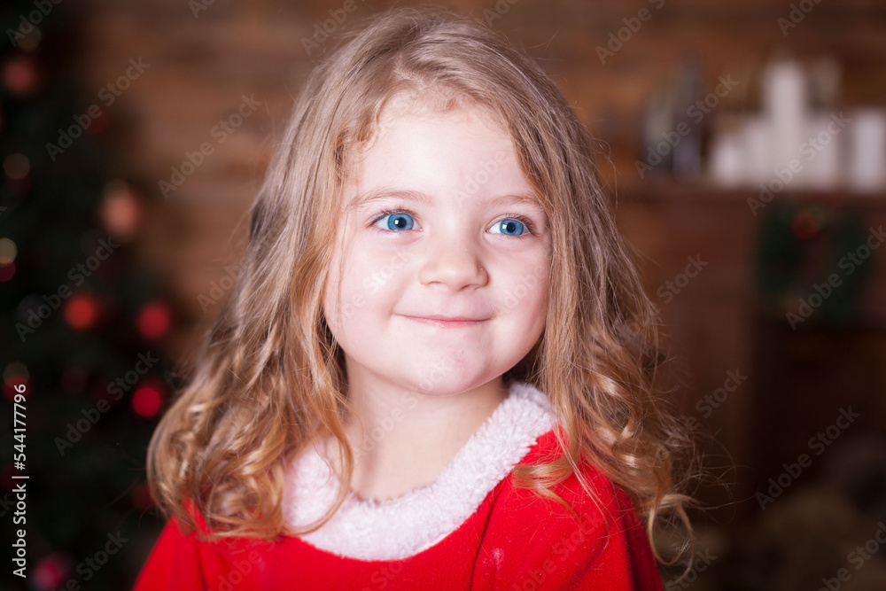 Beautiful little blonde baby girl, has happy fun cheerful smiling face, blue eyes, dressed in red Christmas Santa suit. Kids holiday fashion. Close up. Winter background. Family portrait. Beautiful little blonde baby girl, has happy fun cheerful smiling face, blue eyes, dressed in red Christmas Santa suit. Kids holiday fashion. Close up. Winter background. Family portrait.