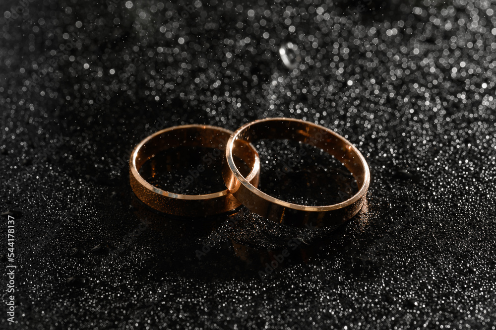gold wedding rings for newlyweds on a wedding day on a black background with water drops. Jewelry gold wedding rings for newlyweds on a wedding day on a black background with water drops. Jewelry