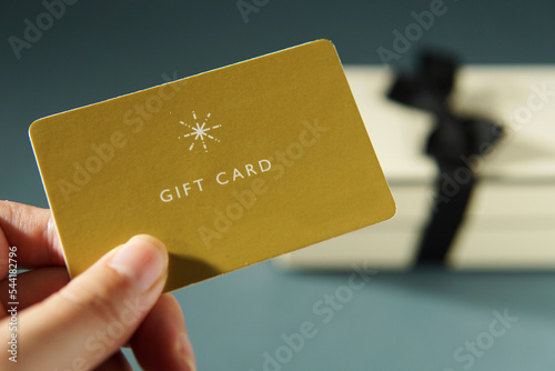 Hand holding a yellow gift card against a gift box background