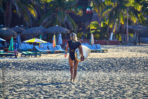 girl walking with a surf board and lounges on the background, zicatela puerto escondido oaxaca 