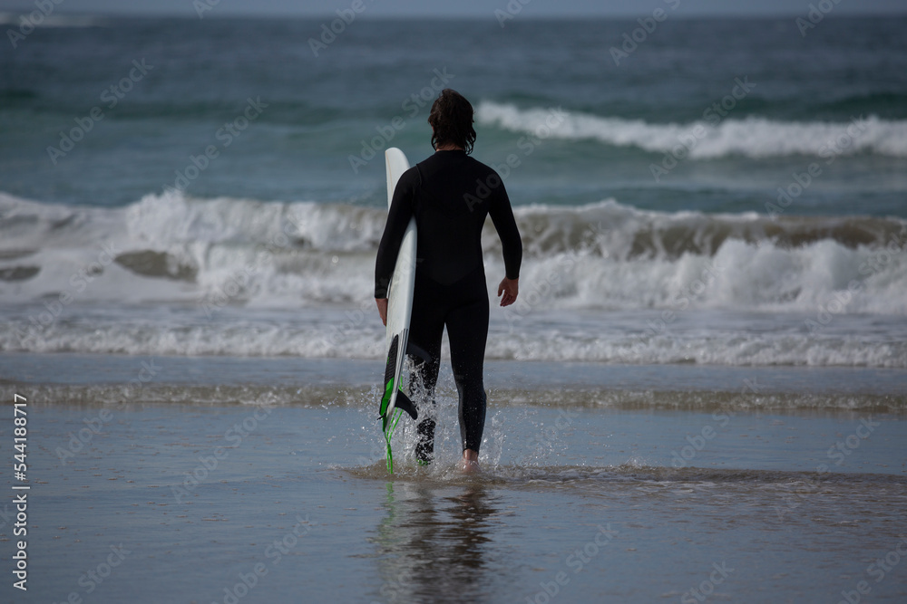 A surfer with a black wetsuit and a white surfboard on the sands of A Lanzada beach, O Grove, Galicia A surfer with a black wetsuit and a white surfboard on the sands of A Lanzada beach, O Grove, Galicia