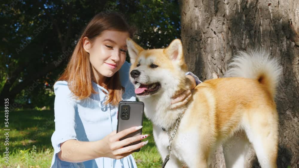 Cute girl takes selfie on smartphone with her dog in park. Young lady ...