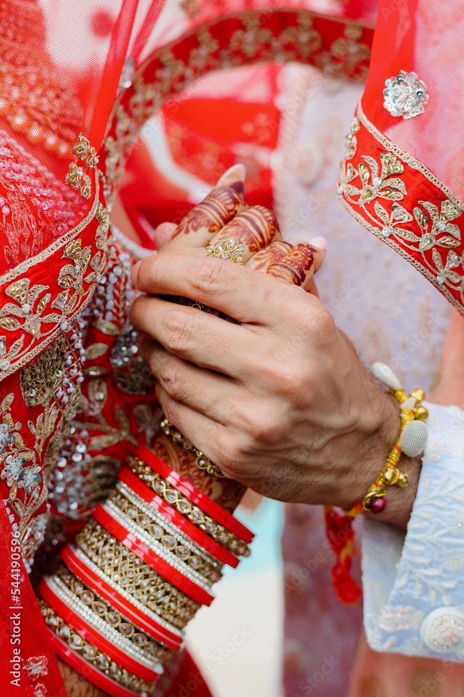 Close up of hands of married loving couple in indian costume. Bring and groom dressed in traditional clothes and accessories holding hands of each other