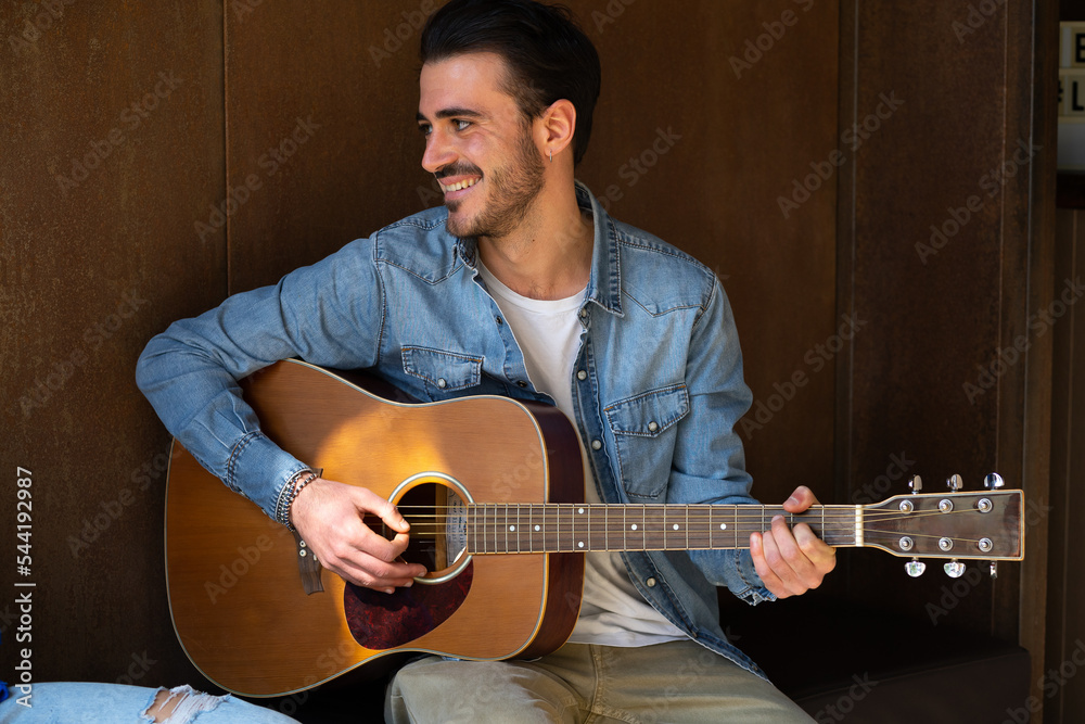 Obraz premium Handsome bearded young man plays guitar smiles and looks away leisure activity