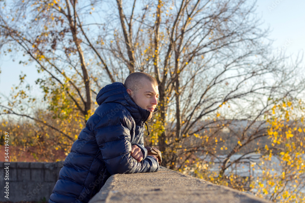 Young Man leaning on the fence and looking at the river, relaxing on a winter sunny day. Young Man leaning on the fence and looking at the river, relaxing on a winter sunny day.
