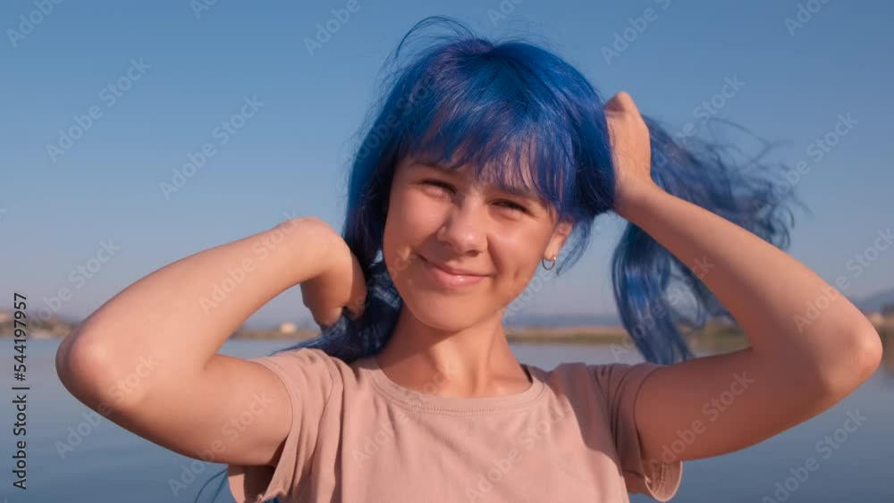Teen with fashion hairstyle on shore. A view of cute teenager with fashion dyed blue hair on the sea shore. A concept of creative tourism and childhood in summer.