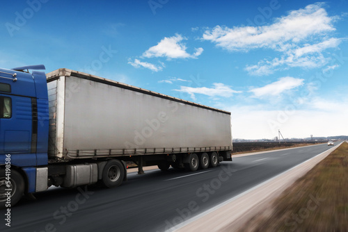 Big truck with a tailer with space for text on a road in motion against a sky with clouds