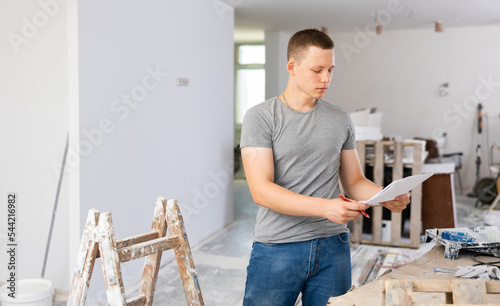 Teenage boy checking documents in construction site during workday on part-time job.