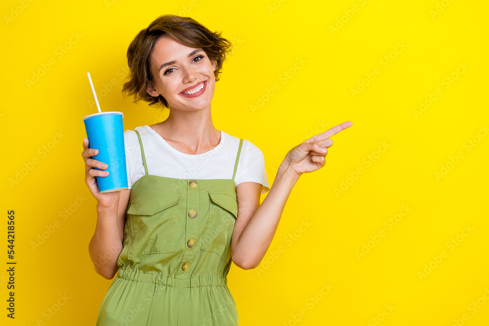 Photo of charming pretty girl wear khaki overalls drinking soda pepsi cola finger directing mockup smiling isolated on yellow color background Photo of charming pretty girl wear khaki overalls drinking soda pepsi cola finger directing mockup smiling isolated on yellow color background