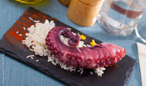 Boiled octopus with rice served on slate with paprika and sauce photo