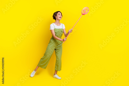 Full body size cadre of funky playful girl wear overalls hold butterfly net catching animals look empty space isolated on yellow color background photo