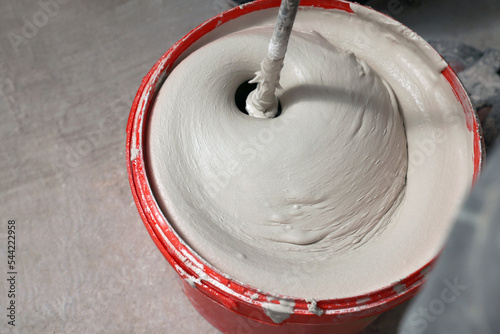 Mixing putty with electric mixer in red bucket indoors, above view photo