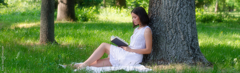 Young woman sitting in the forest and reading book on a beautiful summer day Young woman sitting in the forest and reading book on a beautiful summer day