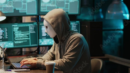 Cyber terrorist with mask hacking database servers, hacker with hood on hacking computer system and activating virus to create malware. Impostor stealing big data, leak information. photo