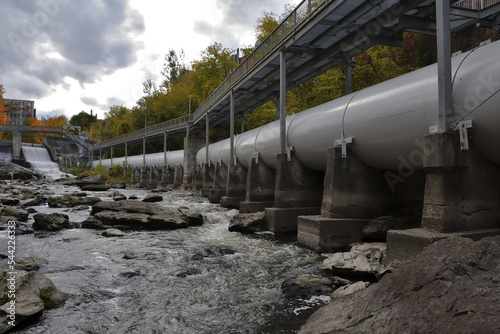 SHERBROOKE, QUEBEC, CANADA - October 10, 2022 Magog river Sherbrooke Abenakis hydroelectric power plant dam. Large white penstock and footbridge photo