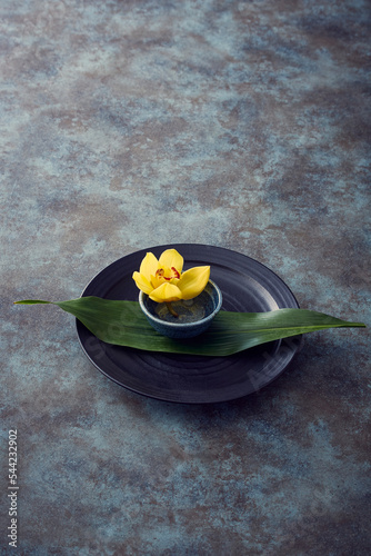 黒い皿に敷かれた葉っぱと小皿に活けられた黄色い花