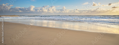 Panoramic view of Cotton Tree surf beach in the golden glow of the early morning after sunrise. The waves are rough and breaking fiercely on the sandy shore.