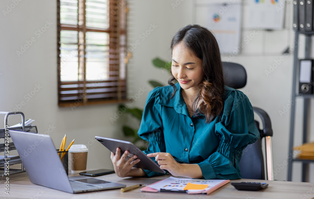Attractive smiling young asian business woman work at home office, Asian woman working on laptop computer holding tablet. Attractive smiling young asian business woman work at home office, Asian woman working on laptop computer holding tablet.