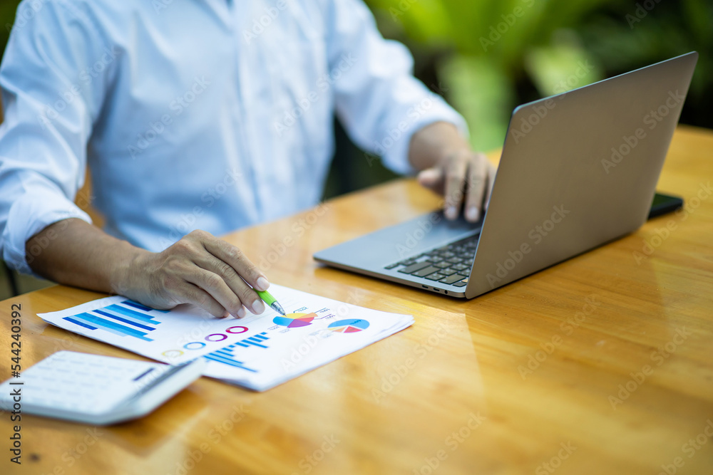 Close-up shot of a man working on marketing analysis Using laptops and smart phones while sitting at a wooden table businessman analyzing documents in hand graph