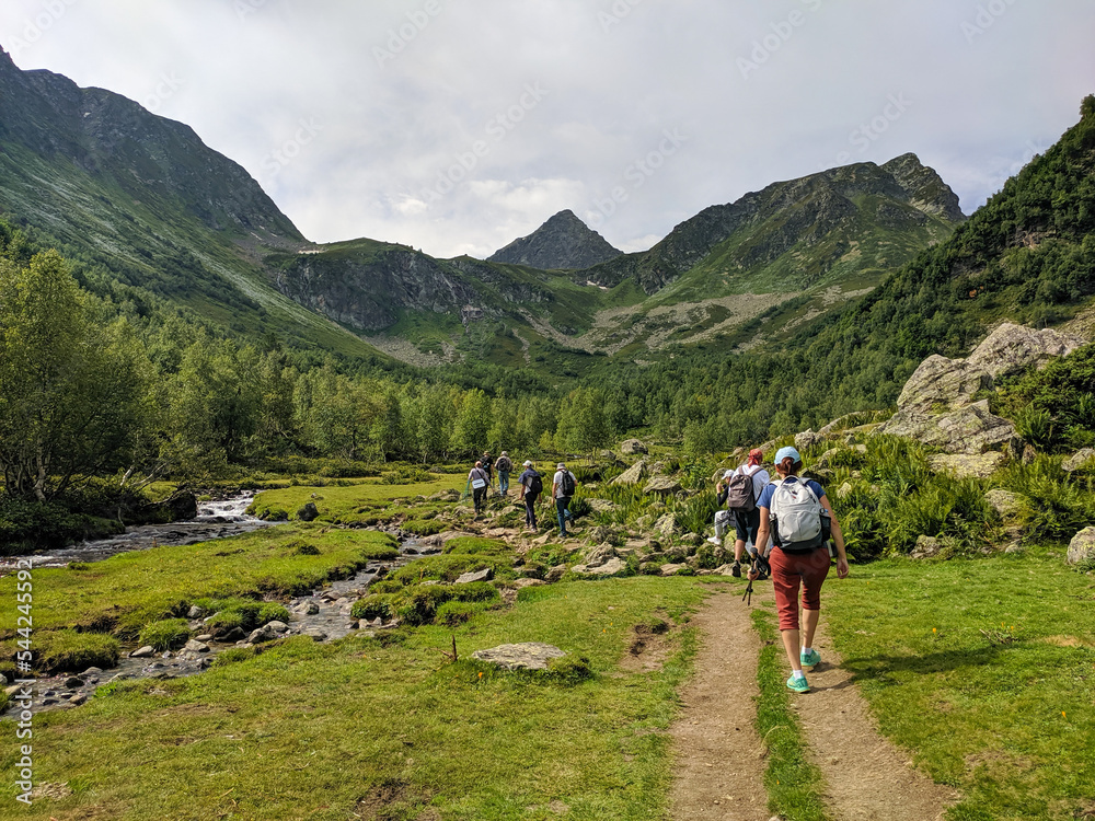 Arkhyz, Karachay-Cherkessia, Russia - August 22, 2022: Beautiful view of the landscape of the Caucasus mountains. People with backpacks in a group cross the stream on the rocks