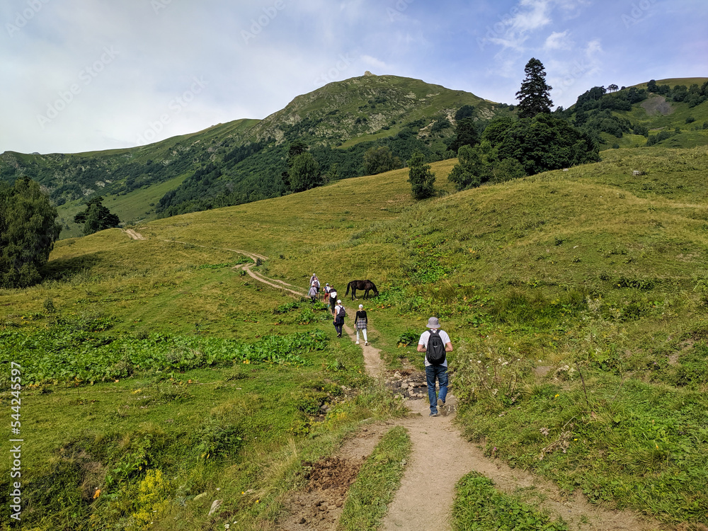 Beautiful view of the landscape of the Caucasus mountains. People with backpacks are walking along the path in a group. Arkhyz, Karachay-Cherkessia, Russia Beautiful view of the landscape of the Caucasus mountains. People with backpacks are walking along the path in a group. Arkhyz, Karachay-Cherkessia, Russia