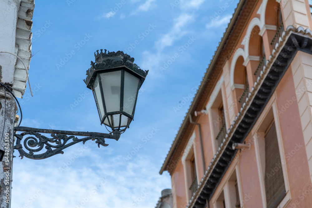 A metal street light hanging outside of a house in a narrow street