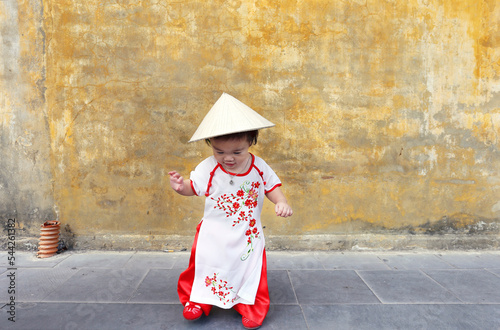 Little Vietnam girl with a vietnamese traditional costume wearing Ao dai walking at Hoi An. Ao dai is famous traditional costume, vintage style, Hoi an Vietnam town.