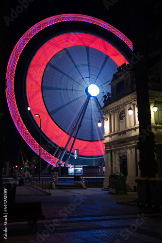 The ferris wheel in the city shines bright lights at night on a long shutter speed.