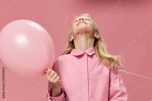a school-age girl stands with her head held high holding a large pink balloon in her hand standing in a pink dress on a pink background with a blank space for an advertising layout © Tatiana