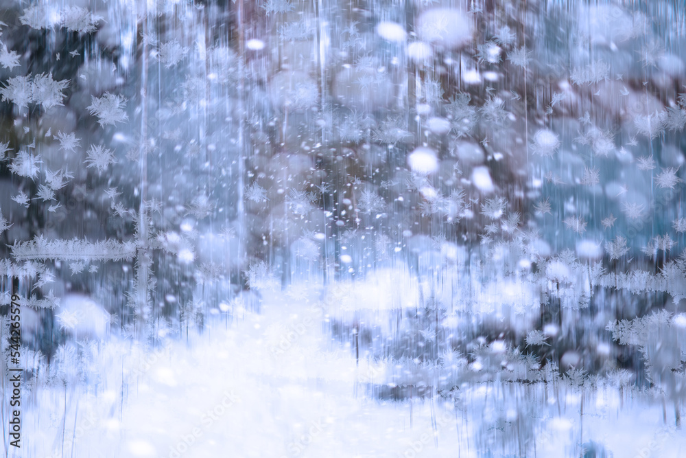 Winter landscape through a frozen window. Blurred snow background. Trees and plants covered with snow.