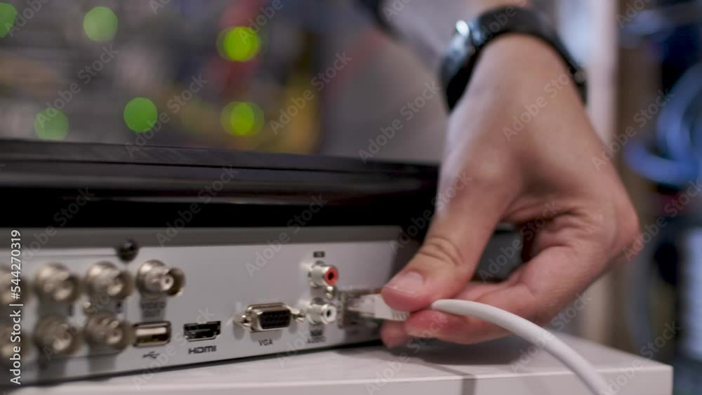 A technician inside the server room, inserting a cable into the LAN port of a computer or router. Handheld closeup shot, detail of the hands.
A technician inside the server room, inserting a cable into the LAN port of a computer or router. Handheld closeup shot, detail of the hands.