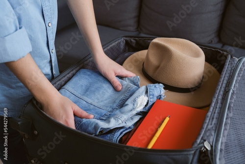 Unrecognizable young woman putting clothes into suitcase ready for trip at home or hotel. Close up side view of female hands packing trunk bag for travel. Tourism summer and adventure concept