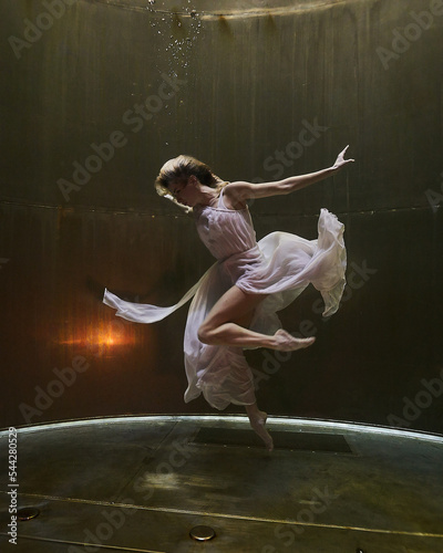 a ballerina dances underwater in a white flowing dress on a dark background in t Fototapet