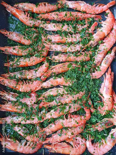 Whole baked red prawns on a baking sheet with herbs. View from above