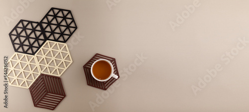 a white cup of green tea on a silicone stand for hot. Nearby there are silicone coasters for hot in different colors. Banner with space for text