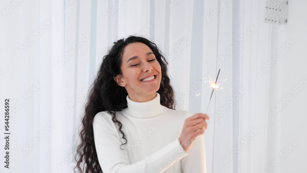 Portrait of happy smiling curly hair latin hispanic woman with holding sparkling fireworks dancing, having fun in front of camera enjoying Christmas holiday, New Year Day in white background. Portrait of happy smiling curly hair latin hispanic woman with holding sparkling fireworks dancing, having fun in front of camera enjoying Christmas holiday, New Year Day in white background.