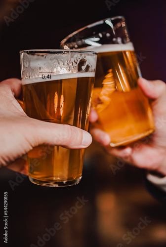 Fotografía Two friends hands clinking glasses of craft beer at the pub or bar