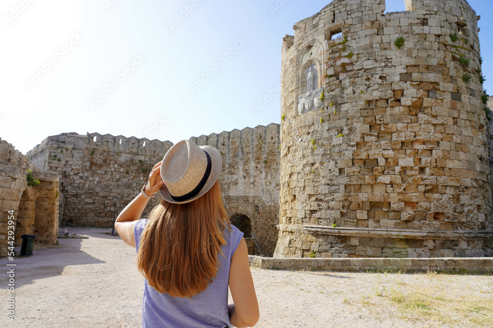 Holidays in Rhodes, Greece. Back view of traveler girl visiting Rhodes fortifications. Young female tourist visiting southern Europe.