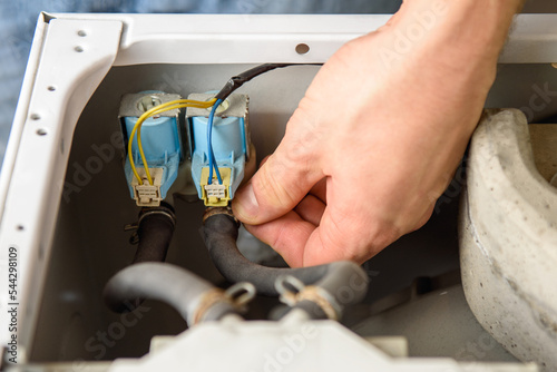 A man is fixing a washing machine. Repairman checks  water inlet valve photo