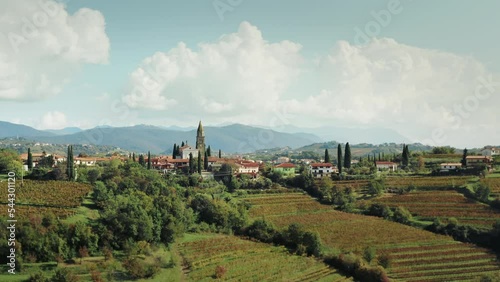 Drone view of a small old village in Italy, Tuscany with a church on a hill surrendered by vineyards at morning light. Wine region with grape plantation and green fields.