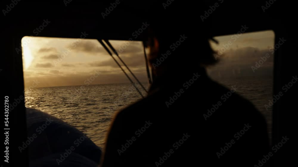 The captain of the ship controls the boat against the backdrop of sunset. The silhouette of a man against the backdrop of a sunset. The water surface is illuminated by the sun. A dramatic sunset with The captain of the ship controls the boat against the backdrop of sunset. The silhouette of a man against the backdrop of a sunset. The water surface is illuminated by the sun. A dramatic sunset with
