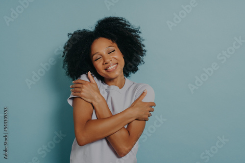 Tableau sur toile Lovely african woman with closed eyes embracing herself while standing indoors a