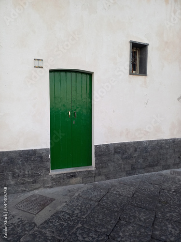Porta verde e finestra con grata, su una facciata bianca di un paesino siciliano photo
