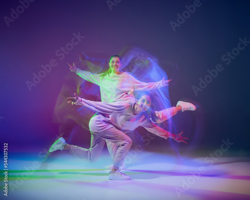 Portrait of young girls dancing hip-hop isolated over gradient blue purple background in neon with mixed light. Performance © Lustre